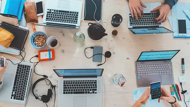 Birdseye view of laptop computers on a spruce table top.